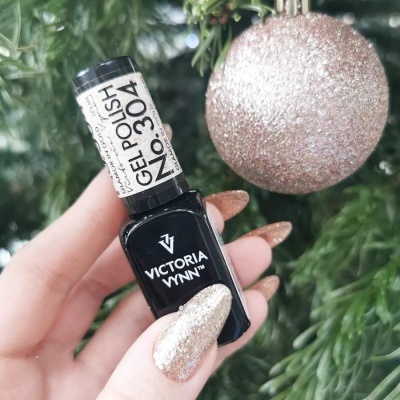 Frasco de verniz gel preto da marca VICTORIA VYNN com unhas glitter dourado e decoração festiva