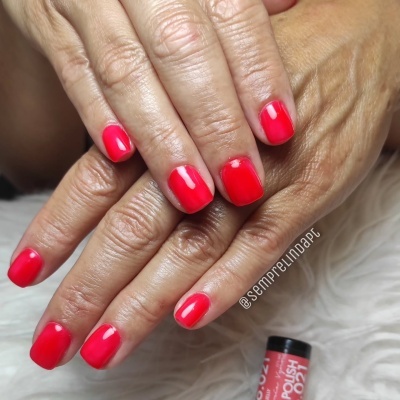 Mãos femininas com unhas vermelhas brilhantes e frasco de verniz