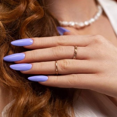 Mão com unhas lilás longas, anéis dourados e colar de pérolas