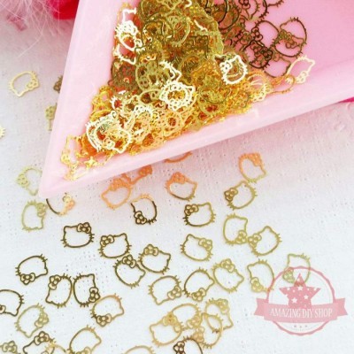 Figuras metálicas douradas em forma de rosto de gato com laço em bandeja rosa e espalhadas numa superfície branca