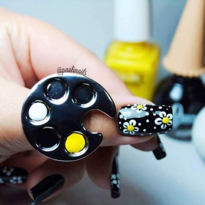 Unhas decoradas em padrão de margaridas e paleta de pintura com tintas amarelas e brancas