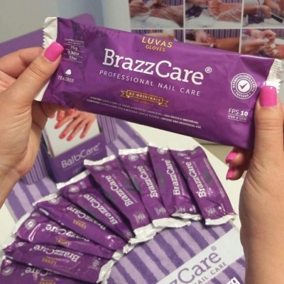 Pacote roxo de luvas BrazzCare nas mãos e vários pacotes semelhantes sobre mesa