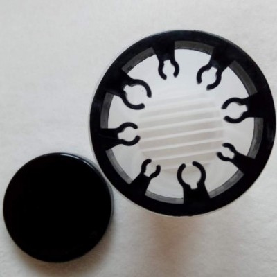 Objeto circular preto com elementos internos translúcidos e tampa preta sobre fundo branco