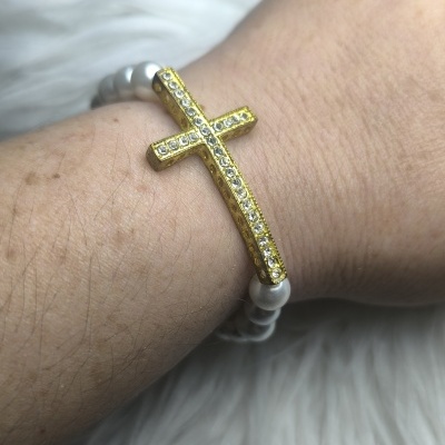 Pulseira de contas de pérola com cruz dourada e cristais no pulso
