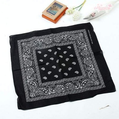 Lenço preto com padrão paisley branco sobre superfície branca com livro e flores