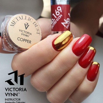 Unhas esmaltadas em vermelho e dourado metálico com frasco de verniz e pó metálico.