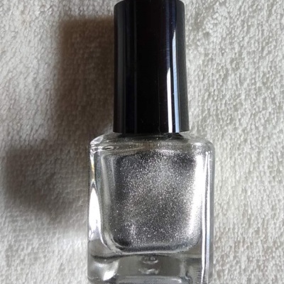 Frasco de verniz de unhas prateado com tampa preta sobre tecido branco