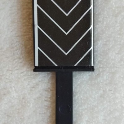 Produto retangular preto com linhas brancas em zig-zag e cabo preto sobre tecido claro