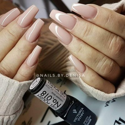 Mãos com unhas quadradas pintadas de verniz nude brilhante segurando frasco de verniz Victoria Vynn