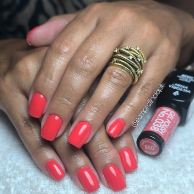 Mãos com unhas vermelhas e anel dourado ao lado de frasco de verniz coral