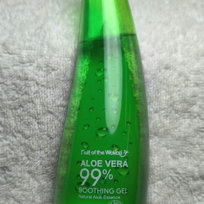 Frasco verde translúcido de gel calmante de Aloe Vera 99% sobre toalha branca.