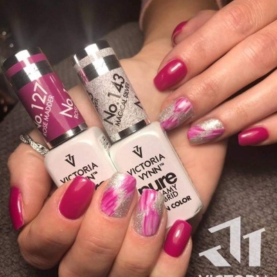 Mãos com unhas pintadas em roxo e branco segurando verniz Victoria Vynn num fundo cinza