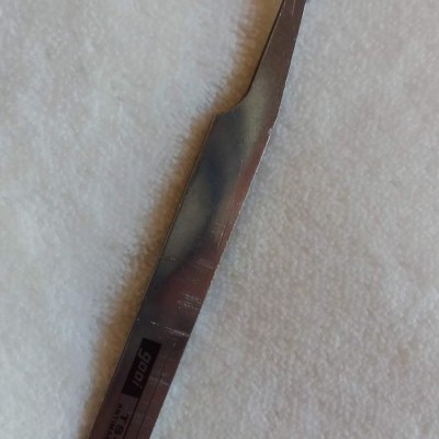 Pinça metálica curva com etiqueta preta e texto '1901', sobre tecido branco