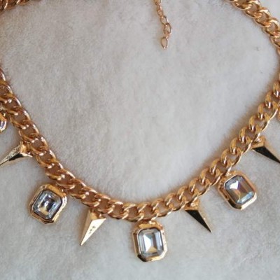 Colar dourado com cristais e espigões sobre tecido branco