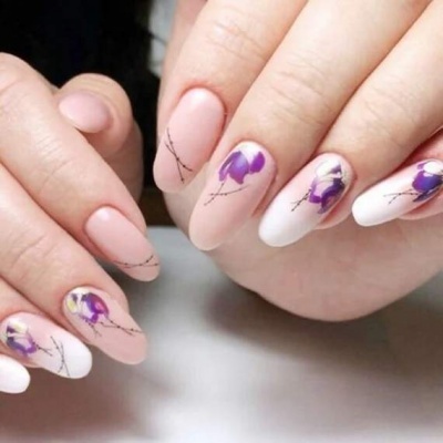 Unhas decoradas com flores roxas e amarelas em fundo nude e branco fosco