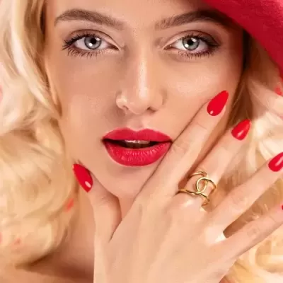 Mulher loira com maquilhagem, unhas e chapéu vermelhos, anel dourado entrelaçado