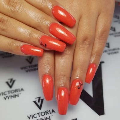 Unhas com verniz laranja brilho e detalhes pretos, sobre papel Victoria Vynn