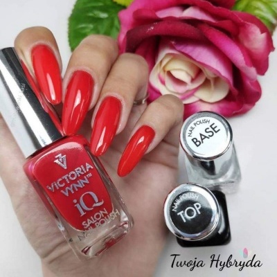 Mão com unhas vermelhas segurando verniz Victoria Vynn, com frascos BASE e TOP e rosa ao fundo