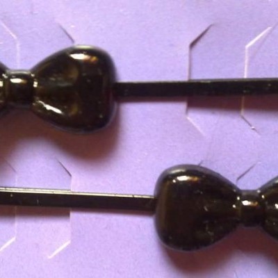 Dois ganchos de cabelo pretos com forma de laço em fundo roxo