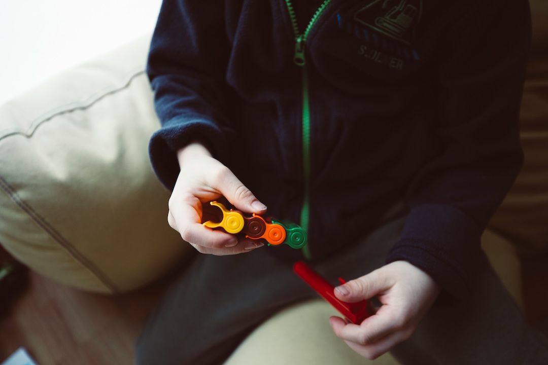 Criança segurando peças coloridas de brinquedo sentada num sofá claro