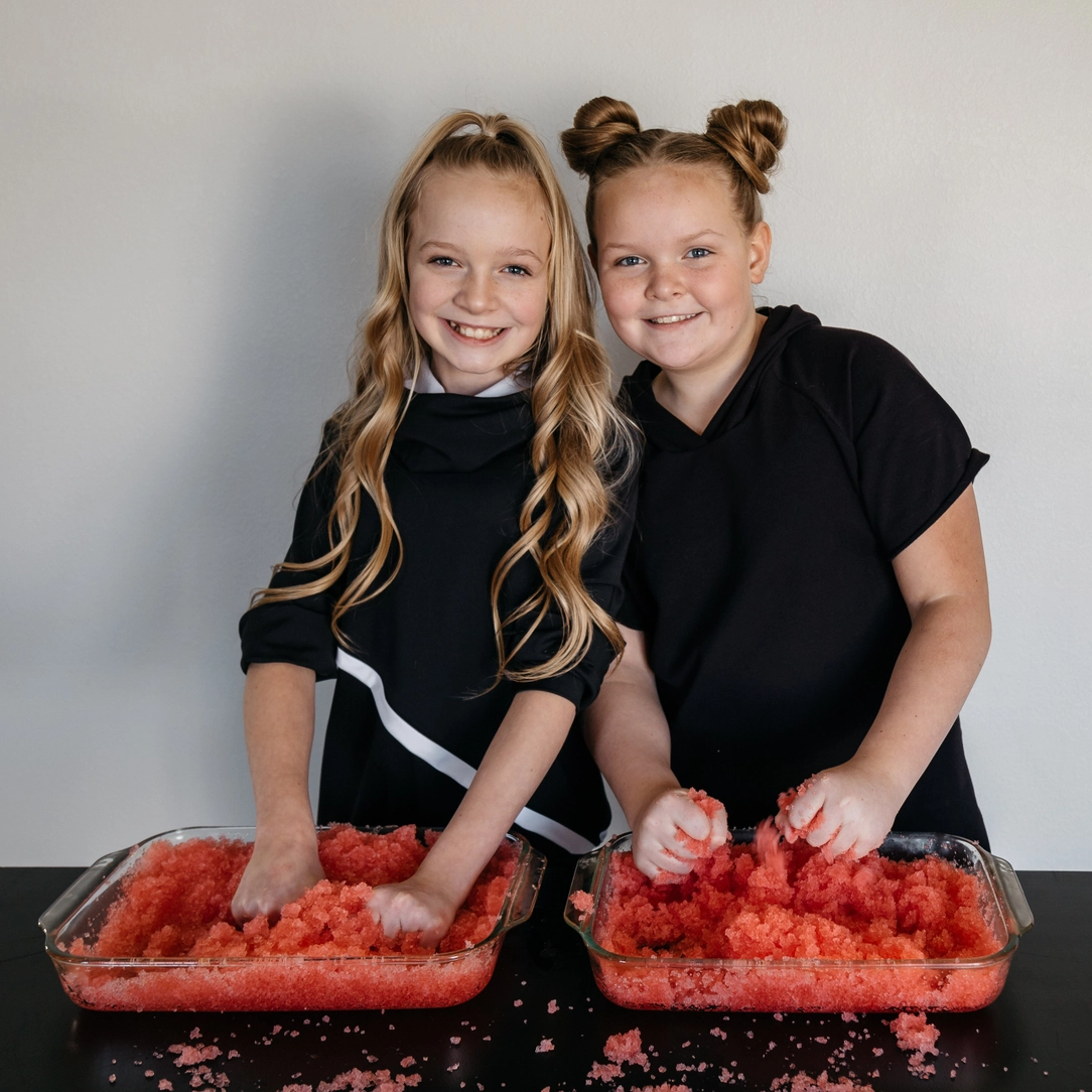 Gelli Play - Gelatina para exploração sensorial Duas raparigas mexem em travessas com material vermelho
