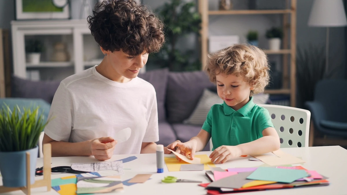 Criança e adulto a fazer trabalhos manuais com papel colorido numa mesa branca numa sala