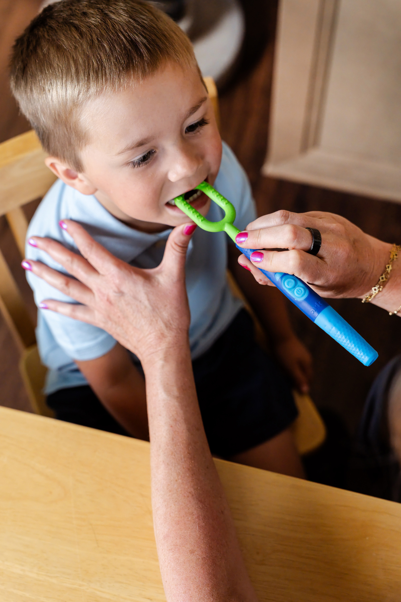 Z-Vibe® Plus da ARK Criança a usar escova dentária azul e verde com adulto, em mesa de madeira