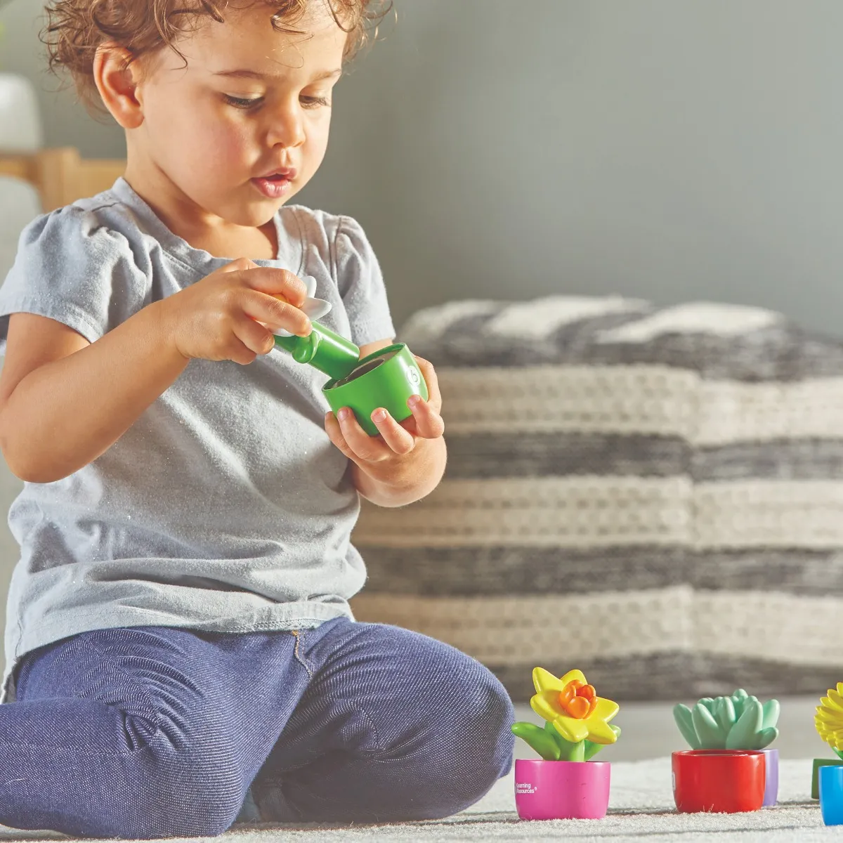 Jardim Shape & Color Criança a brincar com vasos de plantas artificiais coloridas no chão