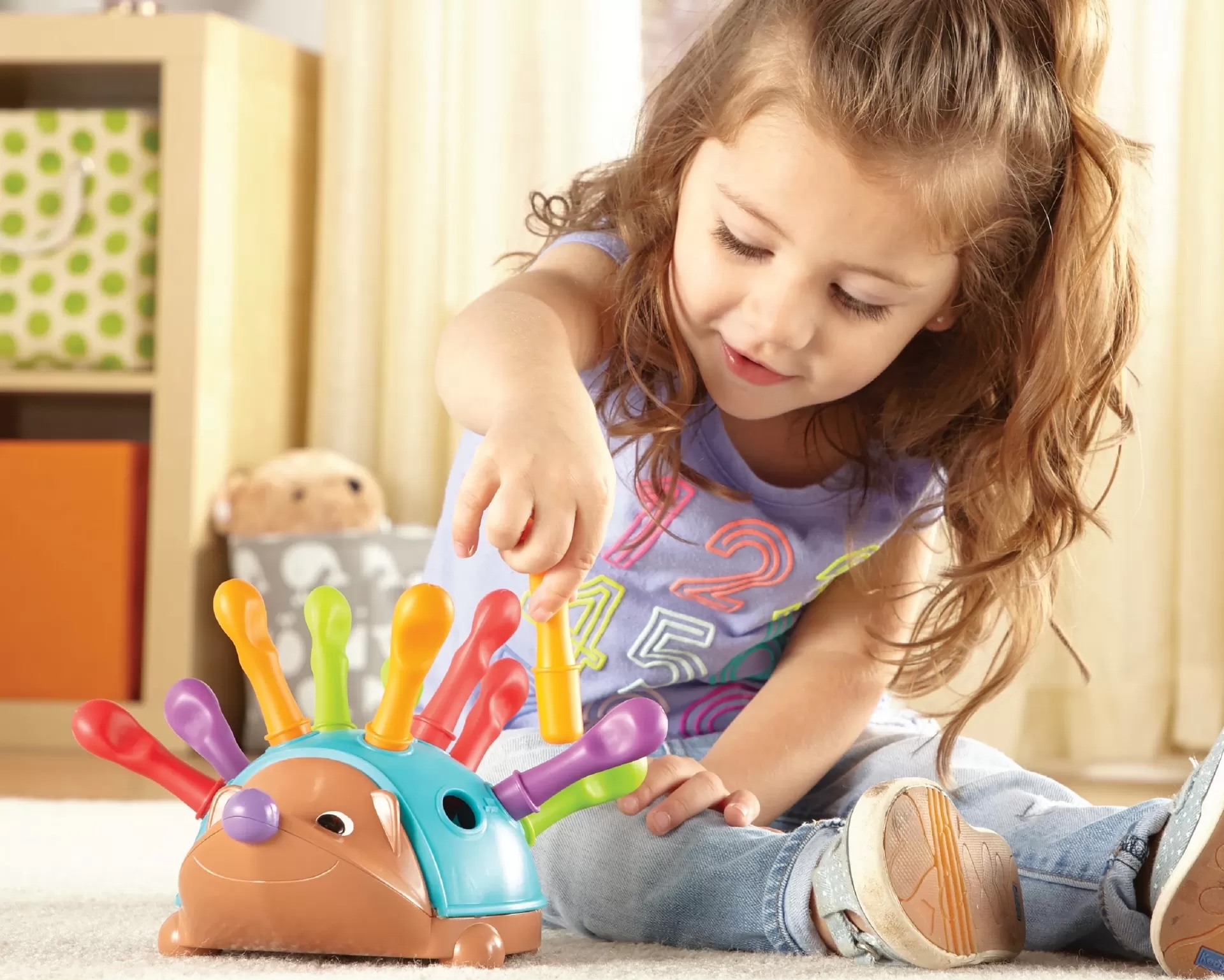Menina a brincar com brinquedo em forma de ouriço colorido no chão