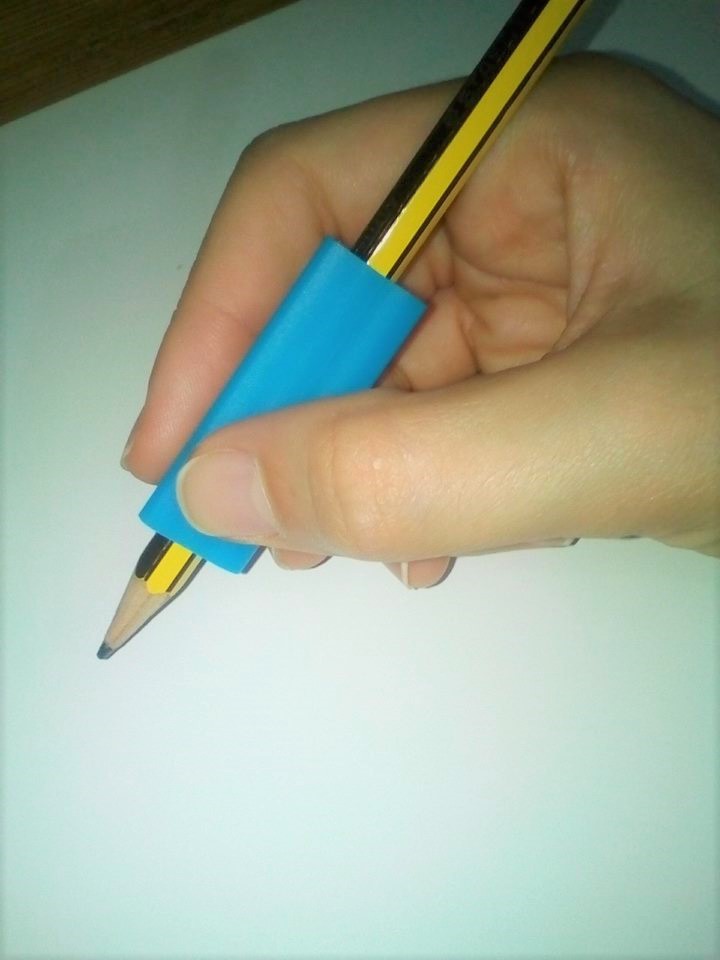 Adaptador para lápis triangular Mão segurando lápis com suporte azul sobre papel branco.