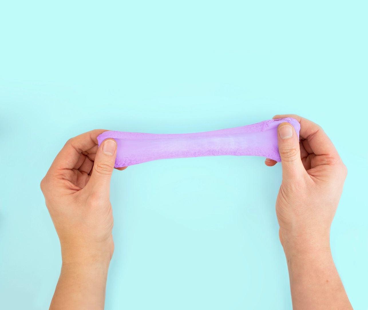 Baff Putty Massa de Moldar Flutuante Brinquedo de slime cor-de-rosa esticado por duas mãos sobre fundo azul