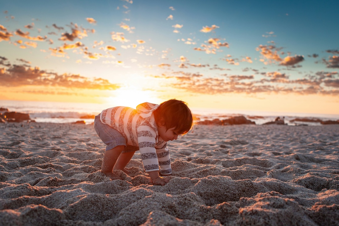 Criança a brincar na areia da praia ao pôr do sol