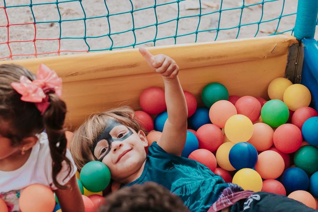 Criança com máscara e camisa azul numa piscina de bolas coloridas