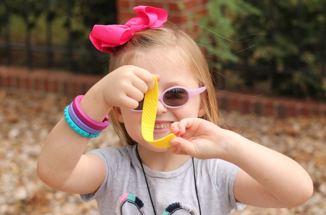 Criança com laço rosa e óculos de sol a segurar brinquedo amarelo
