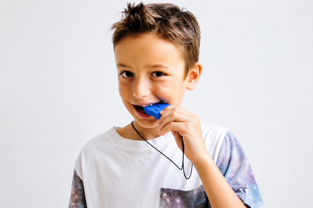 Camisola branca com padrão galáctico nas mangas, menino a morder objeto azul pendurado num colar