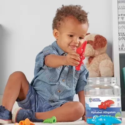 Menino a brincar com crocodilos de plástico coloridos e frasco rotulado Alphabet Alligators.