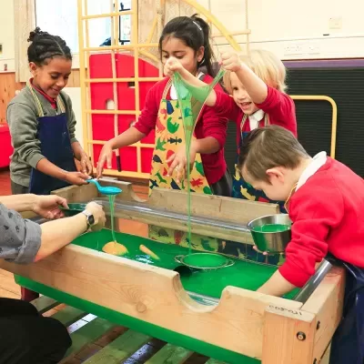 Crianças a brincar com mesa sensorial de líquido verde em ambiente interior escolar