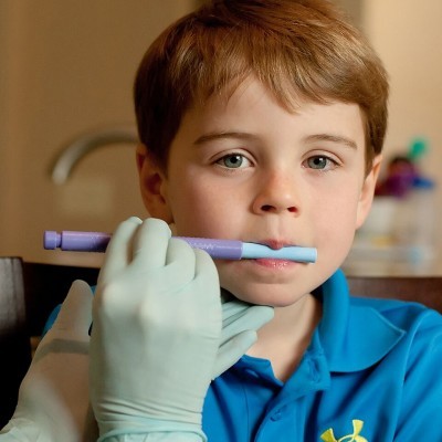 Menino a fazer exame oral com dispositivo roxo e azul por pessoa com luvas brancas