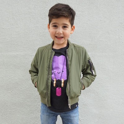 Menino com casaco verde oliva, t-shirt preta com gelado roxo e calças de ganga azuis