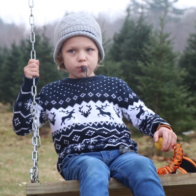 Criança com camisola de renas e gorro sentado num baloiço de madeira