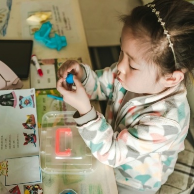 Criança a brincar com massa de modelar azul numa mesa com materiais educativos e acessórios coloridos