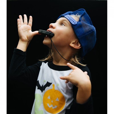 Criança com boné azul a usar apito e t-shirt com abóbora e morcego