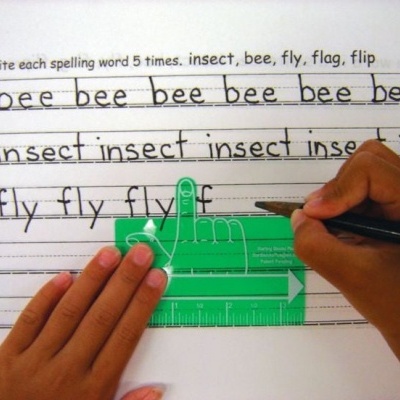 Mãos infantis escrevendo numa folha pautada com régua verde em forma de mão