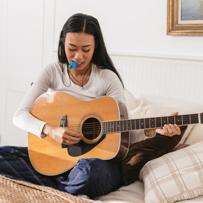 Mulher a tocar guitarra acústica sentada num sofá com almofadas.