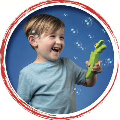 Criança segurando brinquedo de bolhas em forma de crocodilo verde com bolhas ao redor.