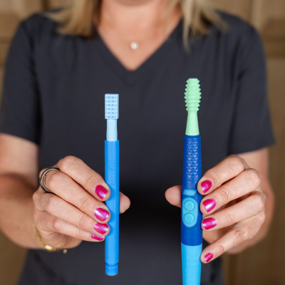 Mulher a segurar duas escovas de dentes de cores azul e verde claro com cerdas de silicone
