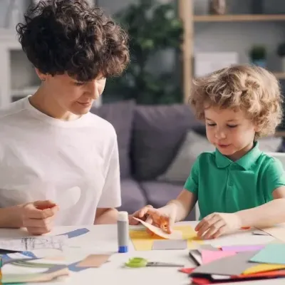 Criança e adulto a fazer trabalhos manuais com papel colorido numa mesa branca numa sala