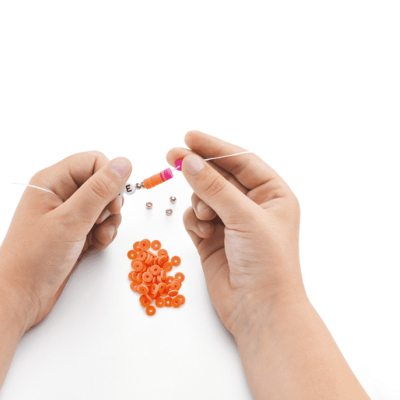 Mãos a enfiar contas coloridas em fio branco com contas laranja e prateadas ao redor