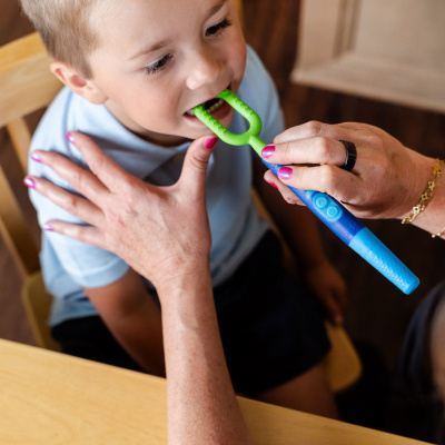 Criança a usar escova dentária azul e verde com adulto, em mesa de madeira
