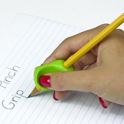 Mão segurando lápis amarelo com apontador verde escrevendo 'The Pinch Grip' num caderno pautado.